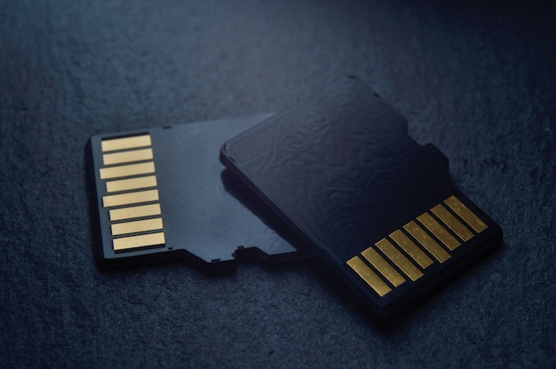 Dos tarjetas micro sd se encuentran una encima de la otra sobre un fondo de textura oscura, con contactos dorados en la parte superior. de cerca.