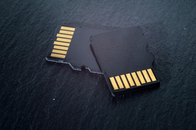 Dos tarjetas micro sd se encuentran una encima de la otra sobre un fondo de textura oscura, con contactos dorados en la parte superior. de cerca.