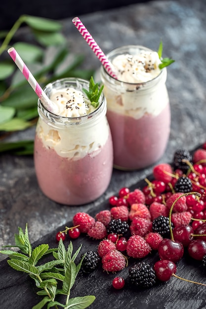 Dos tarros de batido o batido con arándanos, fresas y arándanos sobre la superficie de piedra