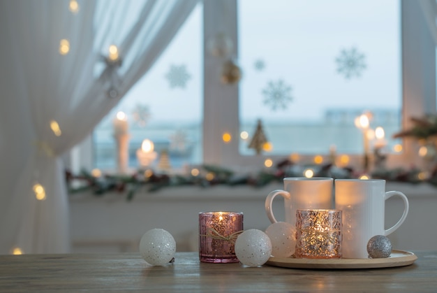 Dos tazas blancas con adornos navideños en la ventana