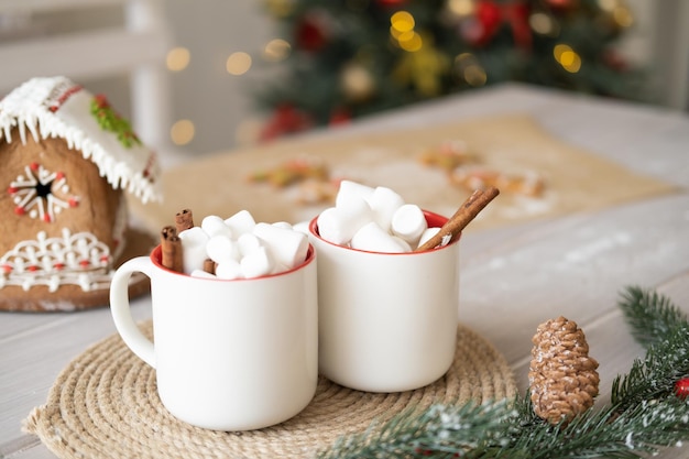 dos tazas blancas de cacao con malvaviscos y casa de pan de jengibre en la mesa sobre el fondo de Navidad t