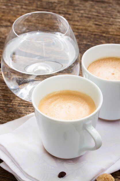 Dos tazas blancas con café expreso y vaso de agua