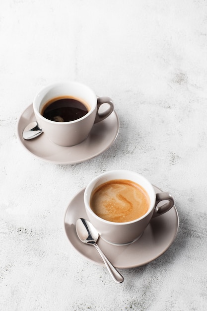 Dos tazas blancas de café negro caliente con leche aislado sobre fondo de mármol brillante. Vista aérea, copia espacio. Publicidad para el menú del café. Menú de cafetería. Foto vertical.