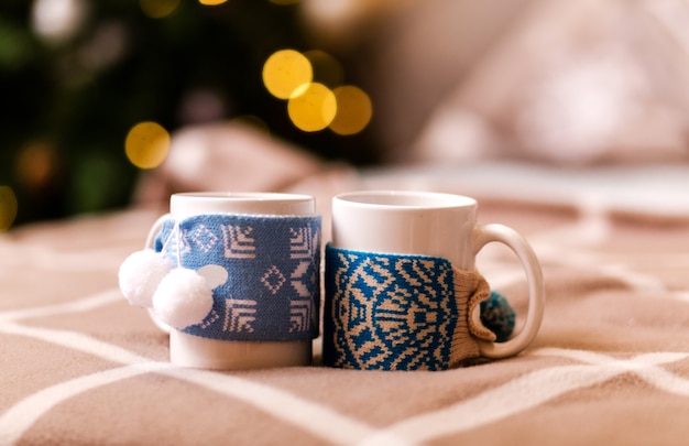 Dos tazas blancas en la decoración de invierno se colocan en una tela escocesa de cuadros marrones contra el fondo de un árbol de Navidad con una guirnalda. Concepto romántico de año nuevo. Foto