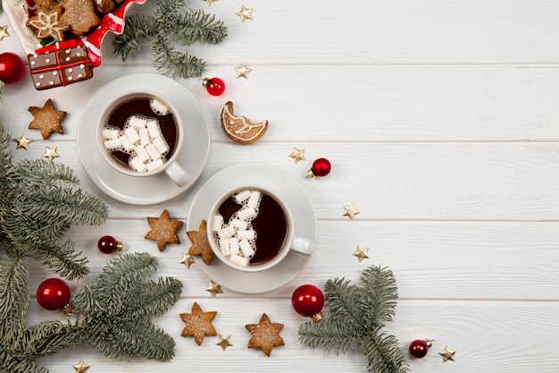 Dos tazas de cacao con malvaviscos y galletas navideñas en un entorno de año nuevo en una madera blanca