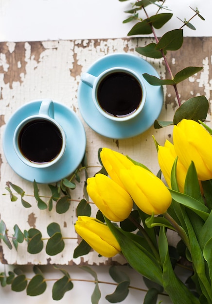 Dos tazas de café azules con tulipanes amarillos en un primer plano de mesa antiguo