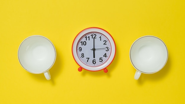 Dos tazas de café y un despertador rojo sobre un fondo amarillo. El concepto de levantar el tono por la mañana.