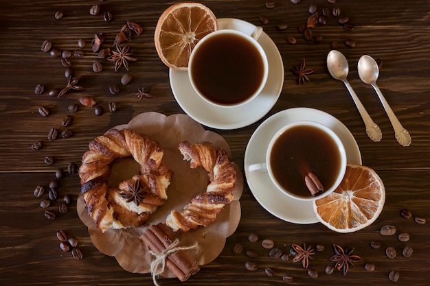 Dos tazas de café y un dulce pretzel rodeado de café y granos de anís. Vista superior sobre madera.