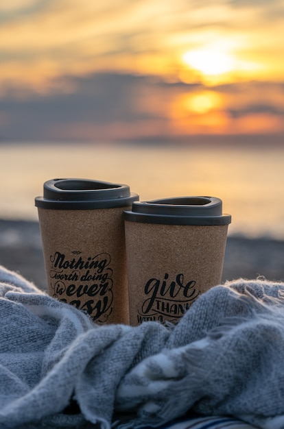 Dos tazas de café en una manta en una playa al atardecer