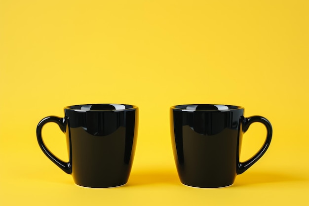 Dos tazas de café negras sobre un fondo amarillo