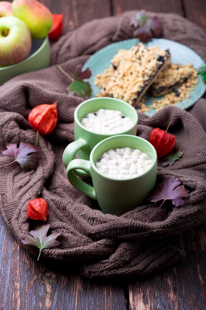 Dos tazas de café o chocolate caliente con malvavisco cerca de manta tejida y pastel.