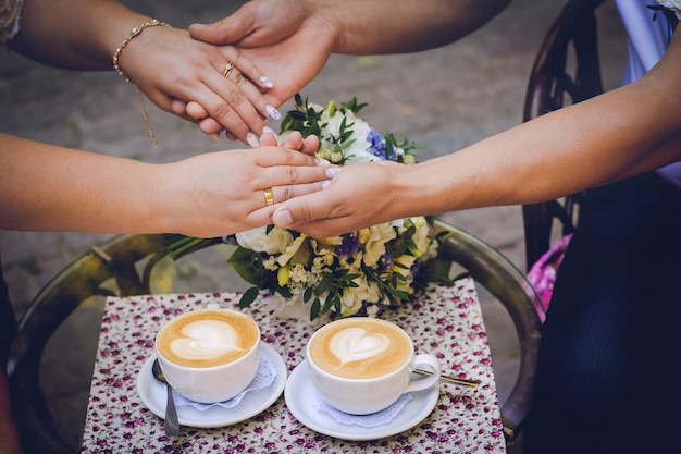 Dos tazas de café y un ramo en la mesa y las manos en las manos