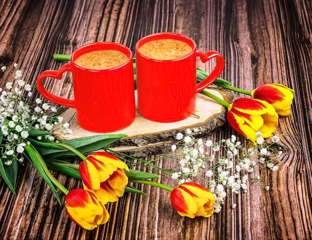 Dos tazas de café rojas con corazones un ramo de tulipanes rojos y flores de gipsófila