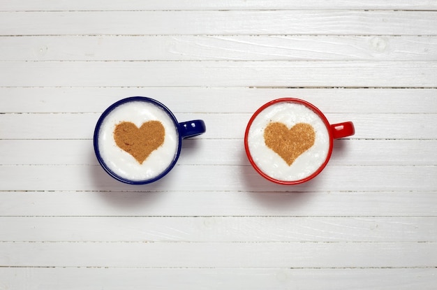 Dos tazas de café con símbolo de forma de corazón sobre fondo blanco de madera