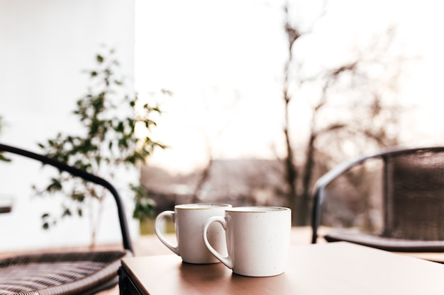 Dos tazas de café sobre la mesa en la terraza de madera marrón durante el atardecer con fondo borroso. Concepto de relajación, cafetería o restaurante.