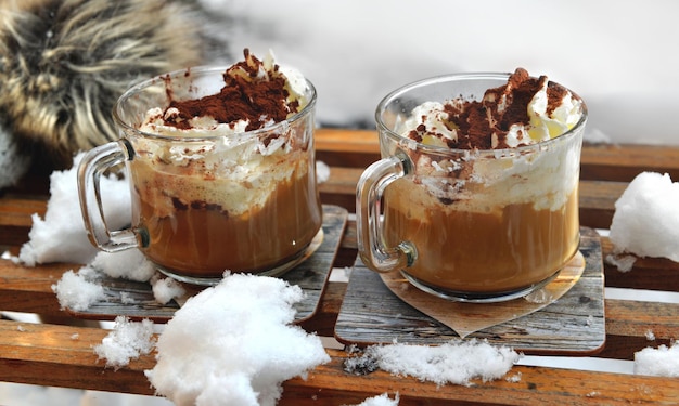 Dos tazas de capuchino colocadas sobre un trineo de madera en la nieve.