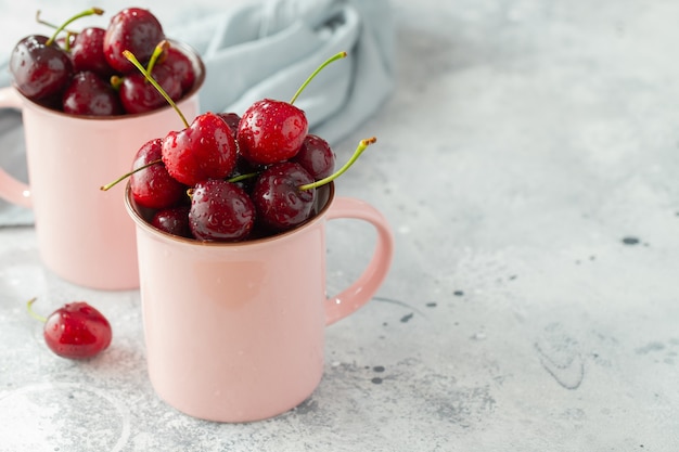 Dos tazas de color rosa con cerezas maduras frescas