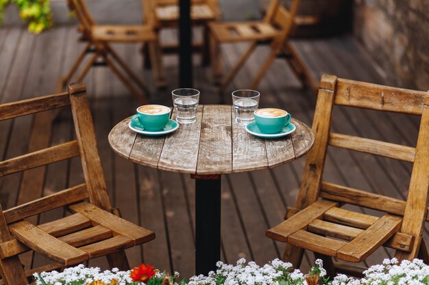 Dos tazas de color verde claro de café aromático caliente con arte latte y vasos de agua servidos en una mesa redonda de madera