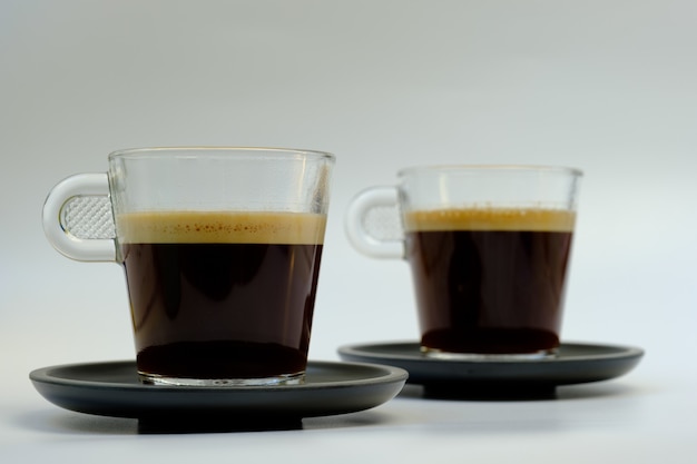 Foto dos tazas de cristal para café en dos platos negros.