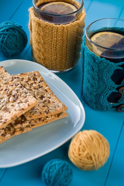 Dos tazas de delicioso té en suéter de punto amarillo sobre fondo azul y galletas