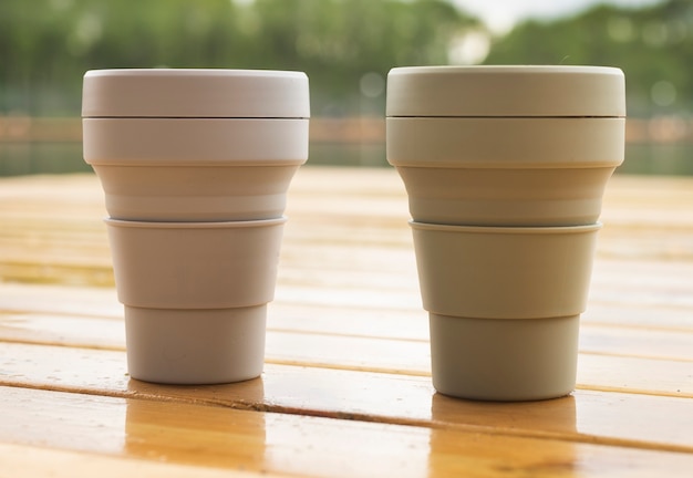 Foto dos tazas ecológicas reutilizables sobre mesa de madera en la naturaleza. estilo de vida sostenible y concepto de cero residuos.