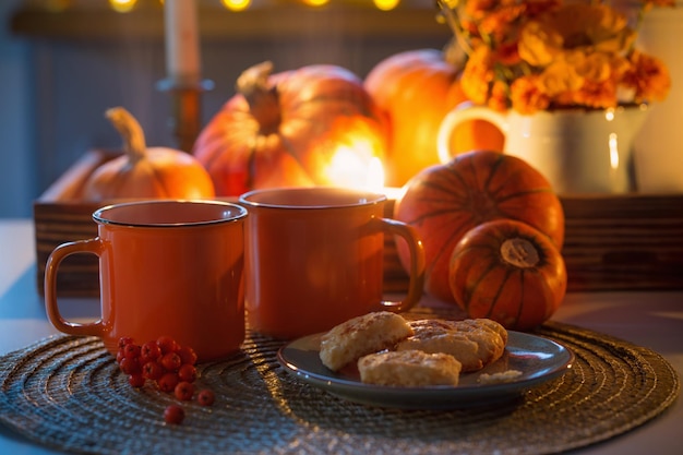 Dos tazas naranjas de té y decoración otoñal con flores de calabaza y velas encendidas en la mesa