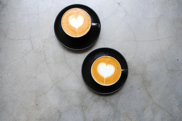 Dos tazas negras de capuchino con arte latte en forma de corazón