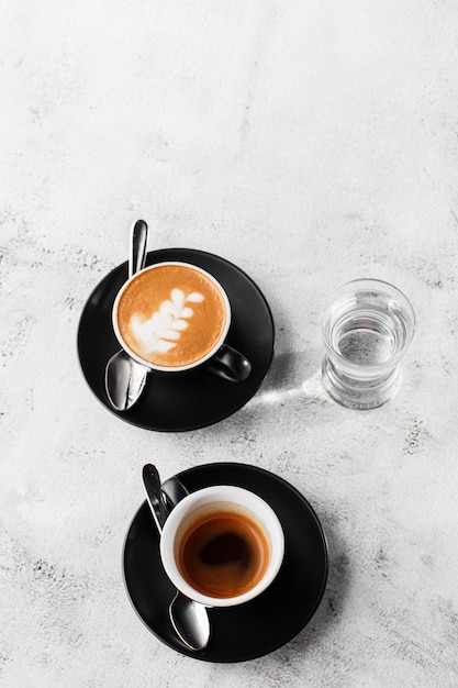 Dos tazas oscuras de café negro caliente, espresso, capuchino con leche aislado sobre fondo de mármol brillante. Vista aérea, copia espacio. Publicidad para el menú del café. Menú de cafetería. Foto vertical.