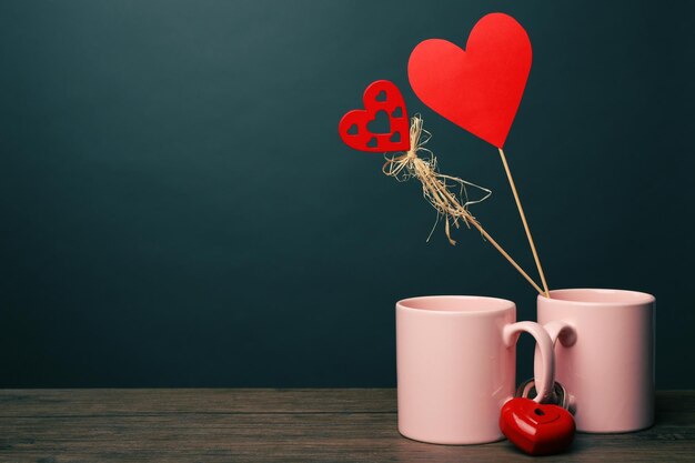 Dos tazas rosas y corazones rojos sobre fondo oscuro