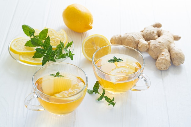 Dos tazas de té de jengibre saludable con menta y limón en el cuadro blanco