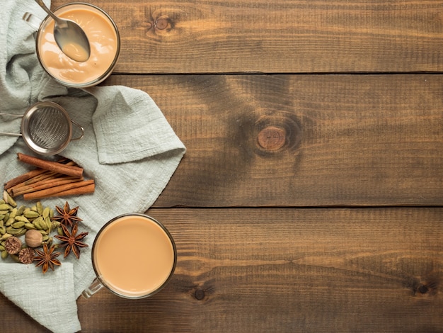 Dos tazas con té masala se colocan sobre una mesa de madera con especias. Vista superior.