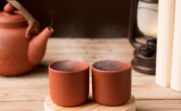 Dos tazas con té o café de arcilla marrón al vapor caliente sobre una mesa de madera con vista parcial de la lámpara