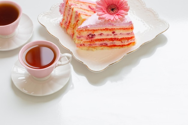 Dos tazas de té con pastel rosa sobre mesa blanca