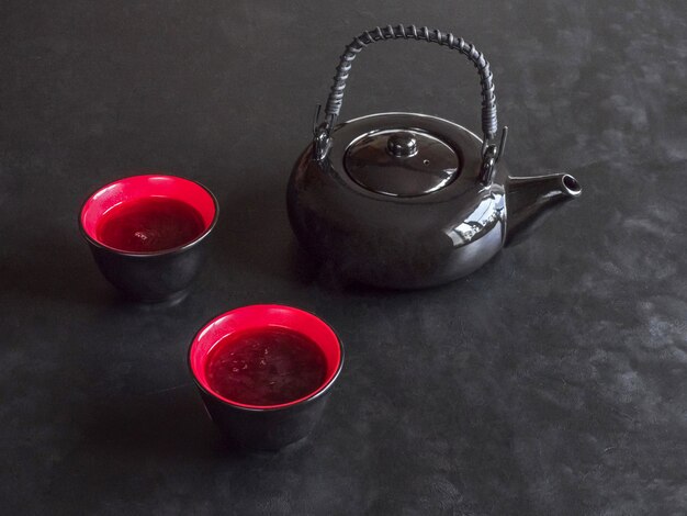 Dos tazas de té rojo y una tetera negra sobre la mesa negra.