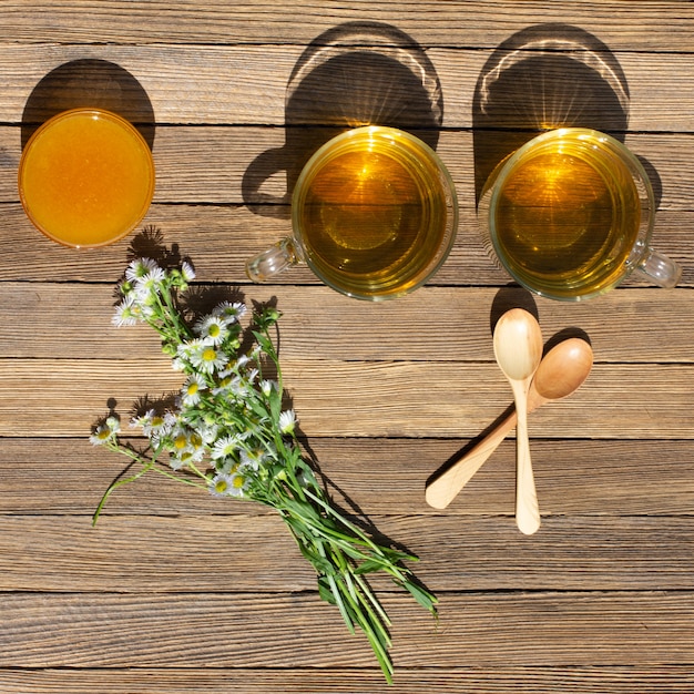 Dos tazas de té verde, miel, un ramo de manzanilla y cucharas de madera sobre la mesa