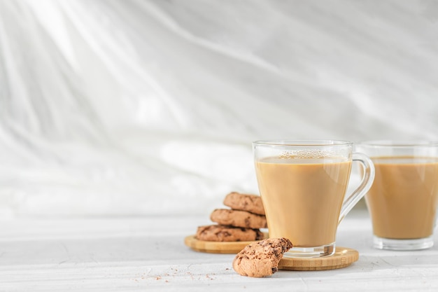 Dos tazas transparentes de café con leche con galletas de chocolate frescas en las sombras de la mañana y los rayos del sol sobre la mesa