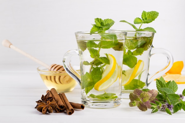 Dos tazas de vidrio té de menta fresca con limón y miel sobre la mesa blanca.