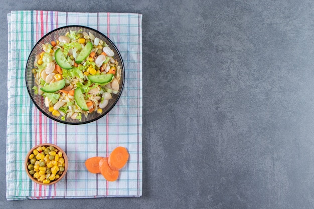 Dos tazones de fuente de ensalada de verduras y zanahoria en rodajas sobre un paño de cocina, sobre la superficie de mármol