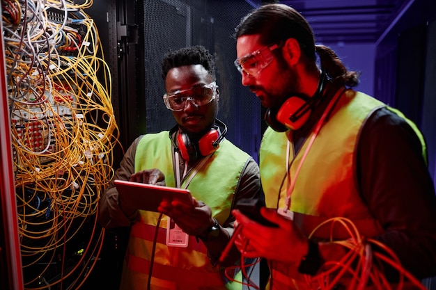 Dos técnicos de red que usan una tableta mientras reparan el servidor con luz de neón