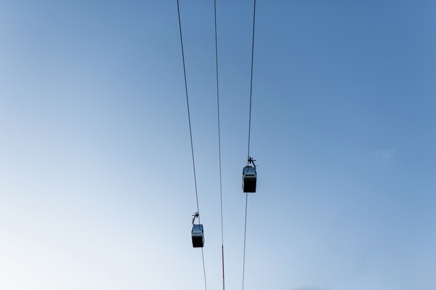 Dos teleféricos eléctricos sobre un fondo de cielo azul claro. Recurso. Descanso extremo activo. Vista desde abajo.