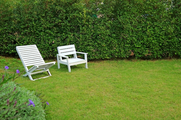 Dos tipos diferentes de sillas de madera de color blanco en un jardín verde vibrante