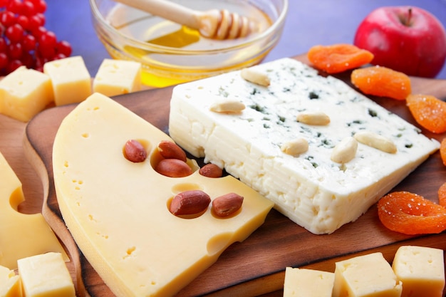 Dos tipos de queso con frutas, bayas, nueces y frutos secos sobre una tabla de madera. Varios tipos de composición de queso con miel y panecillos sobre un fondo azul.