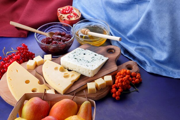 Dos tipos de queso en una tabla de madera con frutas y bayas de cerca Quesos con miel sobre un fondo azul con servilletas azules y rojas