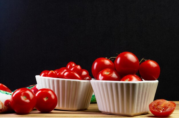 Dos tipos de tomate dentro de un tazón blanco sobre una mesa de madera con fondo negro