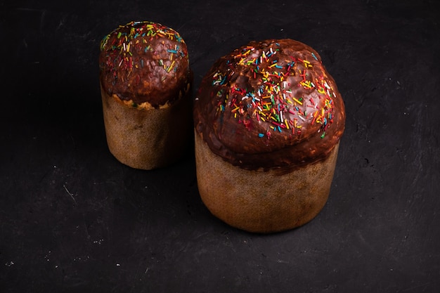 Dos tortas de Pascua espolvoreadas con chocolate y espolvoreadas con dulces de pie sobre una superficie negra