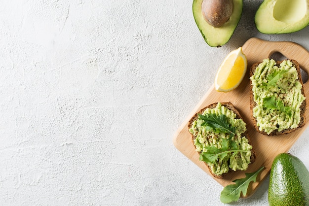 Dos tostadas con aguacate y ensalada verde en el desayuno sobre fondo blanco.