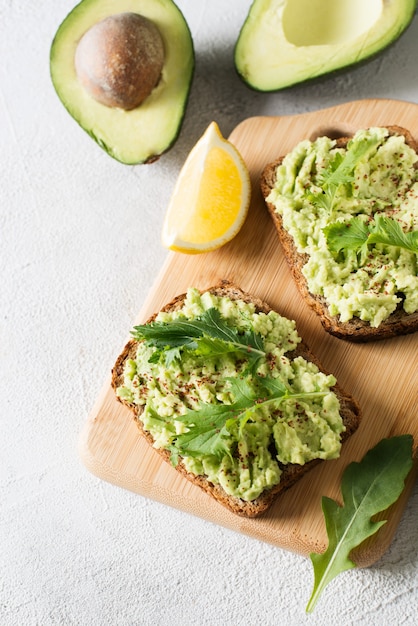 Dos tostadas con aguacate y ensalada verde en el desayuno sobre fondo blanco.