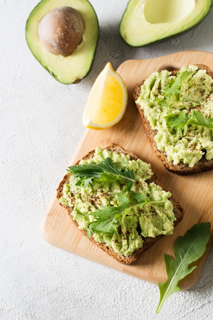 Dos tostadas con aguacate y ensalada verde en el desayuno sobre fondo blanco.