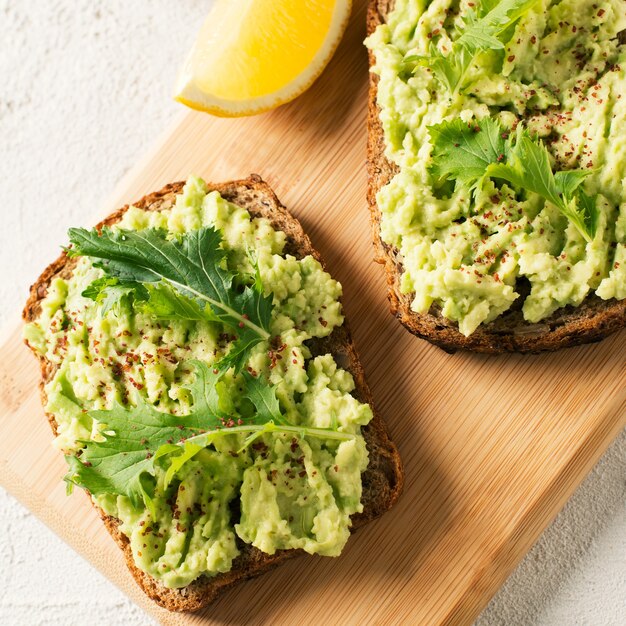 Dos tostadas con aguacate y ensalada verde en el desayuno sobre fondo blanco.