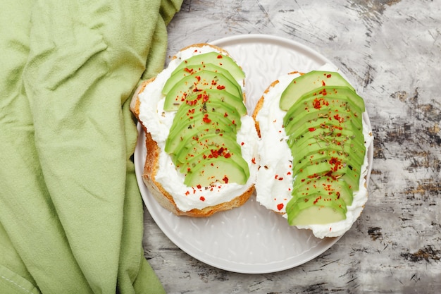 Dos tostadas de aguacate en placa gris, sándwich de aguacate. Aguacate fresco rebanado sobre una tostada de pan de trigo, queso crema, aguacate espolvoreado con especias de chile